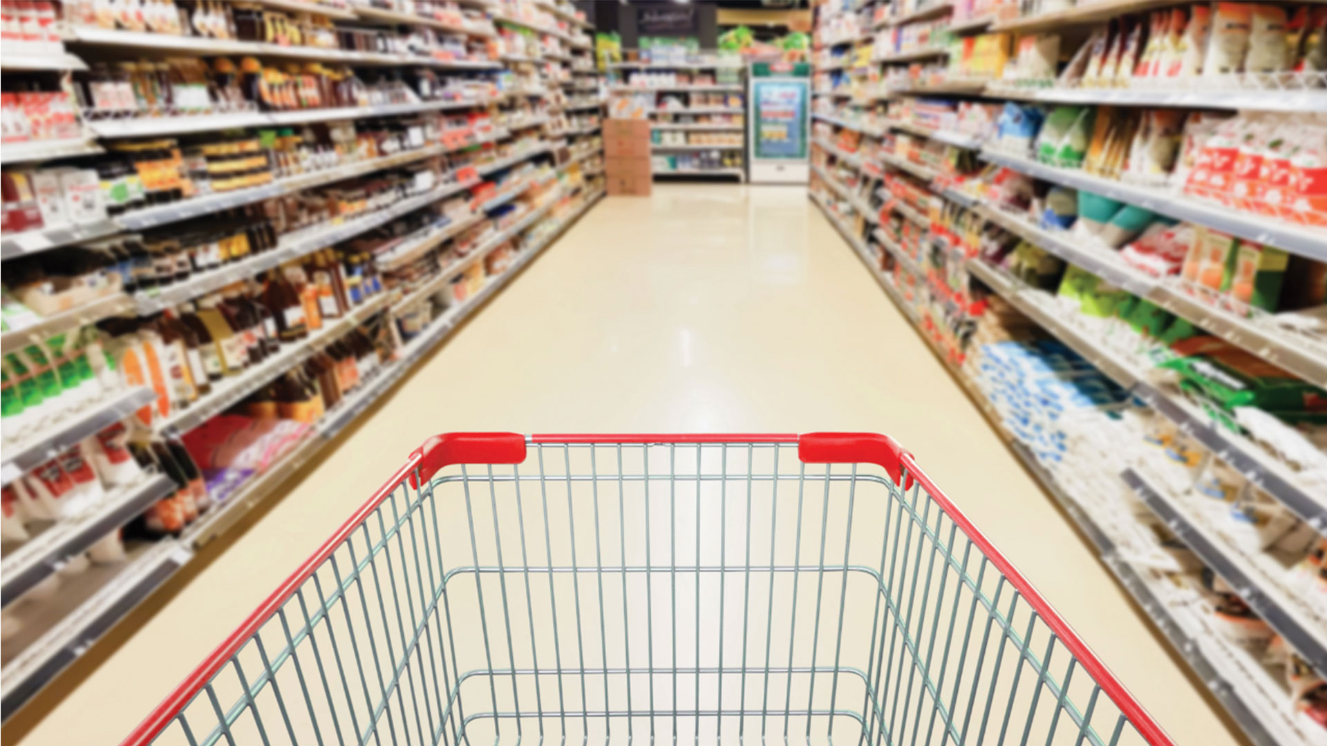 Shopping cart with red accents in the foreground of a grocery store aisle